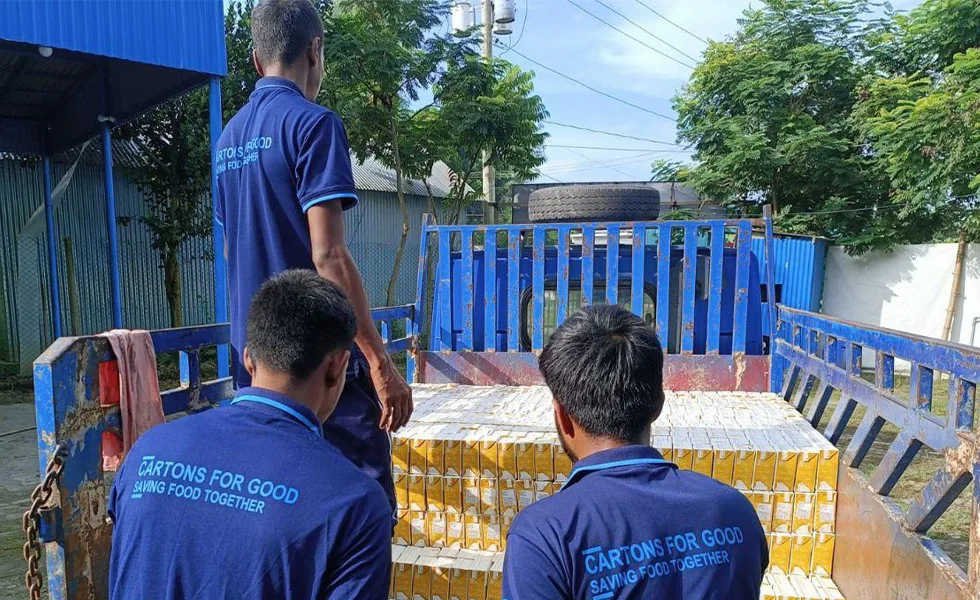 The image features a group of three men standing around a large pile of SIG packaging units. They appear to be workers, possibly discussing their next steps. The signs on their shirts read 