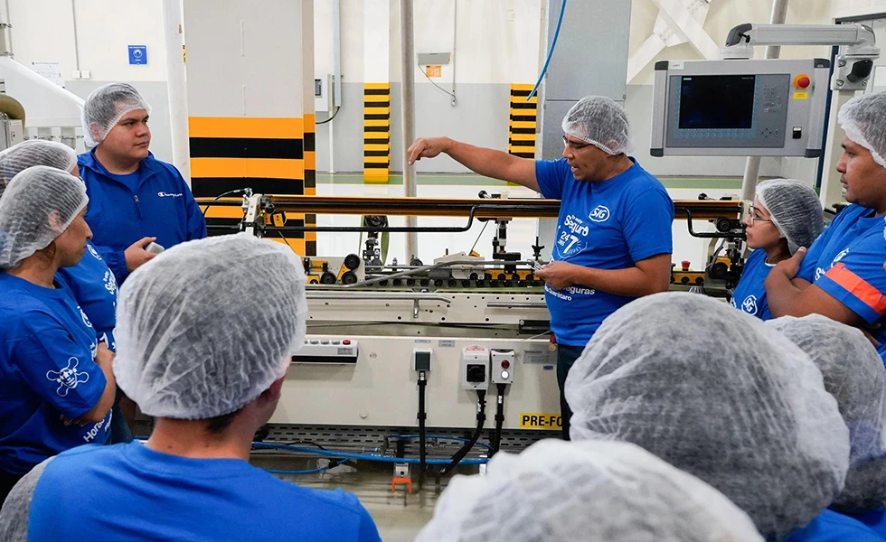 Workers in hairnets listening to a demonstration on a factory floor (photo)